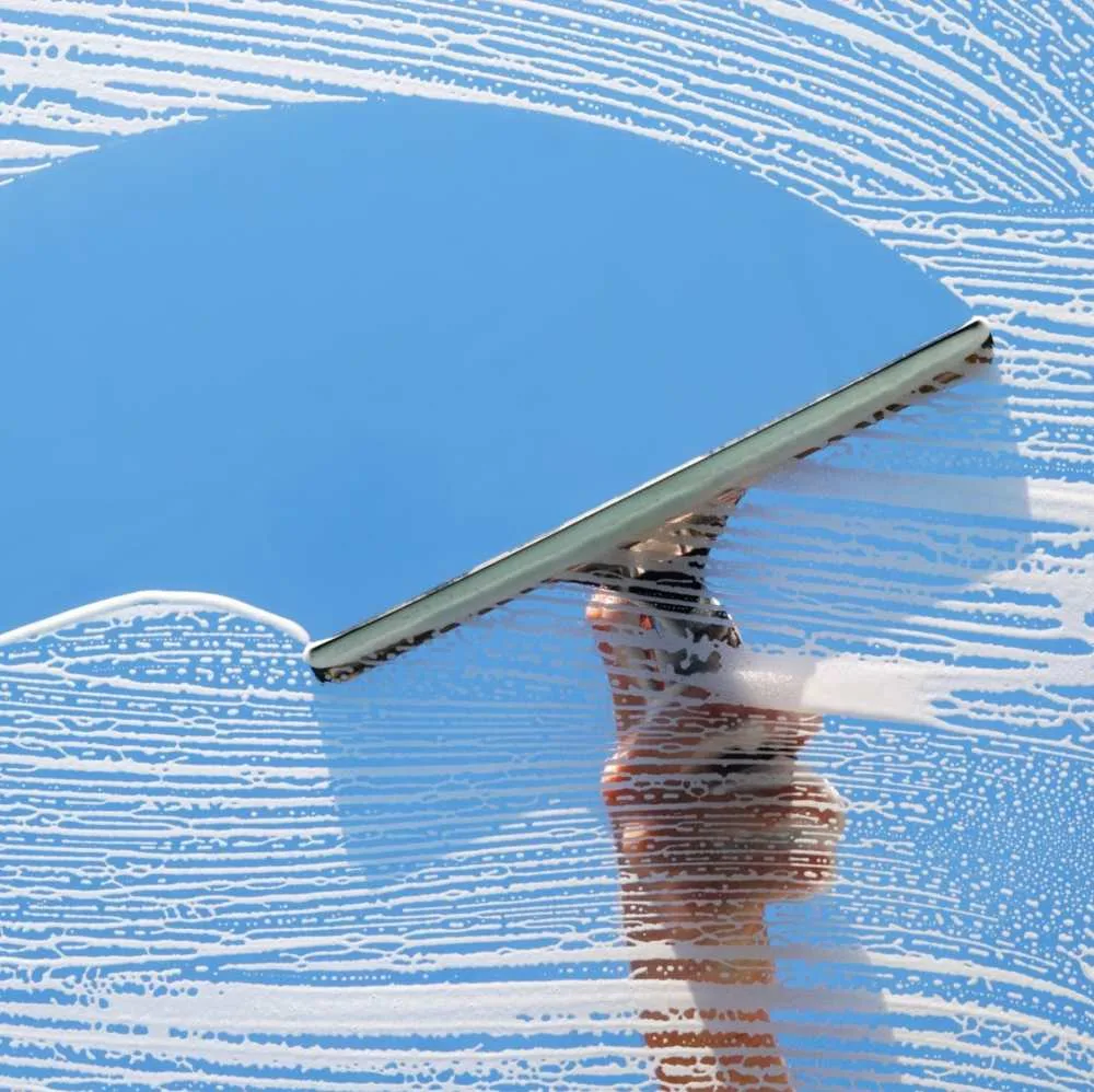 Gloved hand drawing a squeegee down a wet residential window pane, leaving clear glass behind the blade
